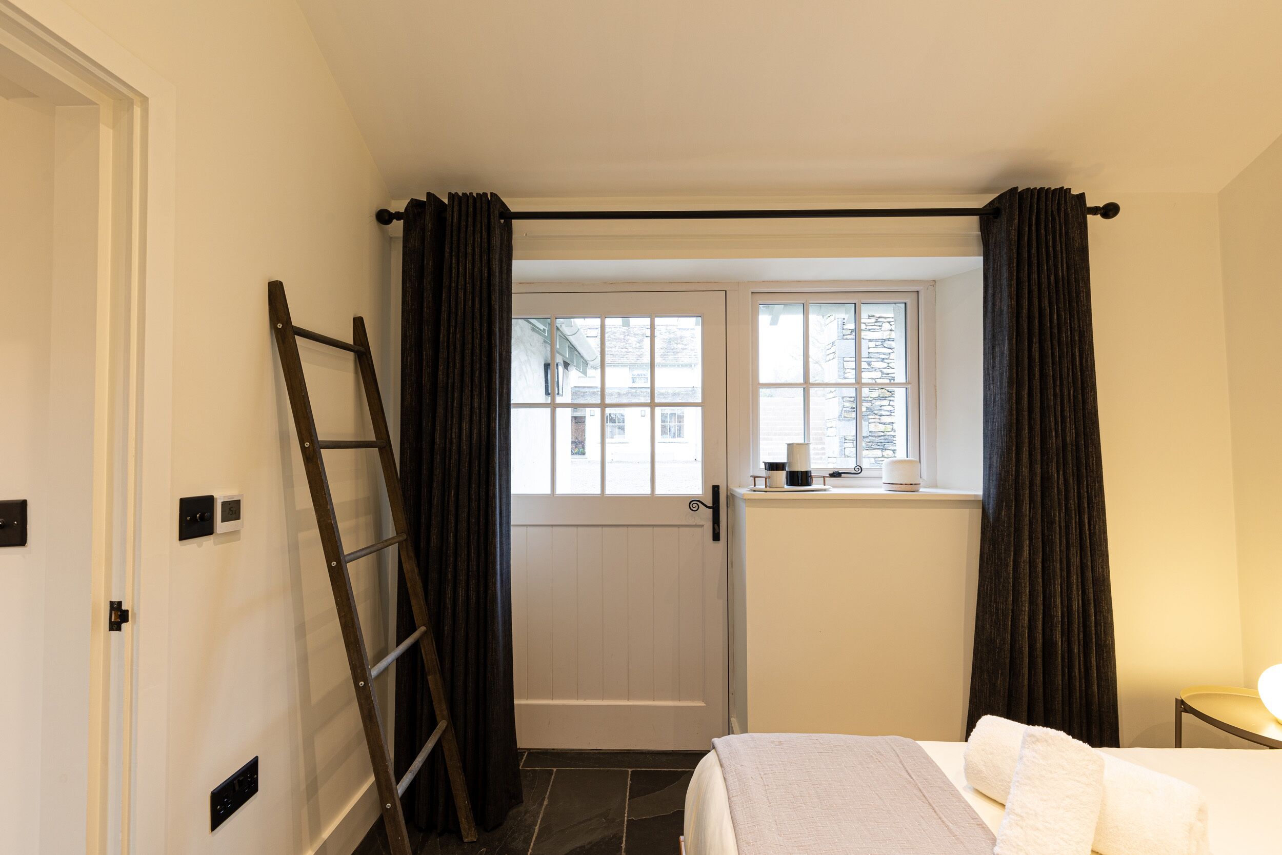 Une chambre à coucher avec un lit, une fenêtre avec des rideaux, une porte et une échelle.