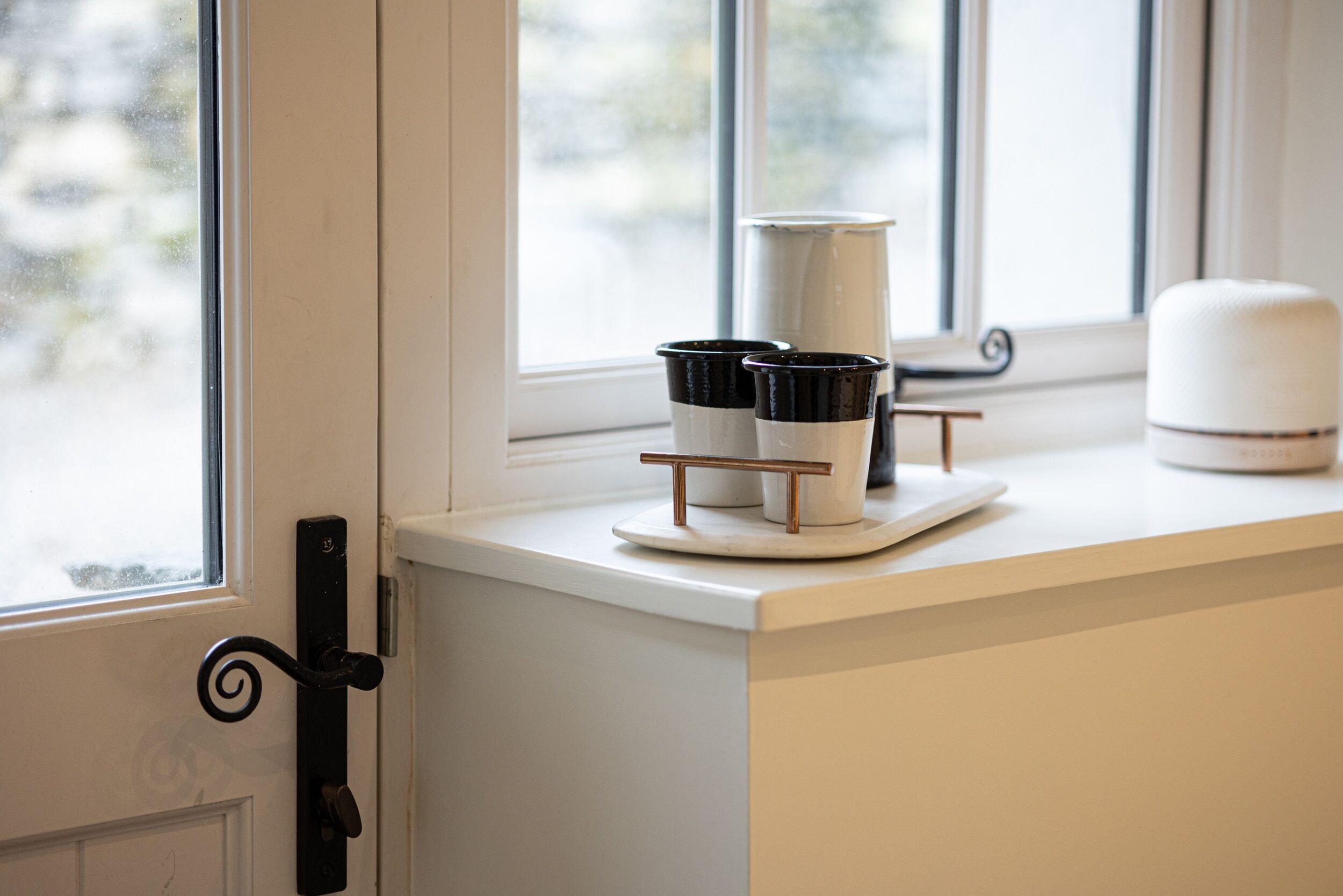 A kitchen counter with a coffee maker, a set of black and white cups, and a white container.
