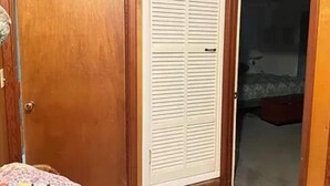 Una habitación con una puerta de madera, un armario blanco con puertas persianas y una cama con colcha estampada.