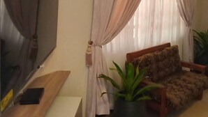 A living room with a flat-screen TV, a sofa, a coffee table, and a potted plant. - Fresh Air Lodge (Accra)