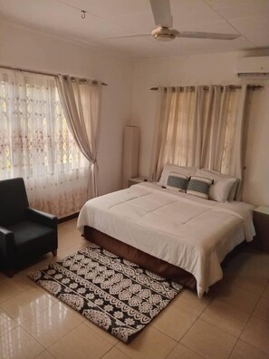 Quarto com cama, uma cadeira, tapete estampado e cortinas.