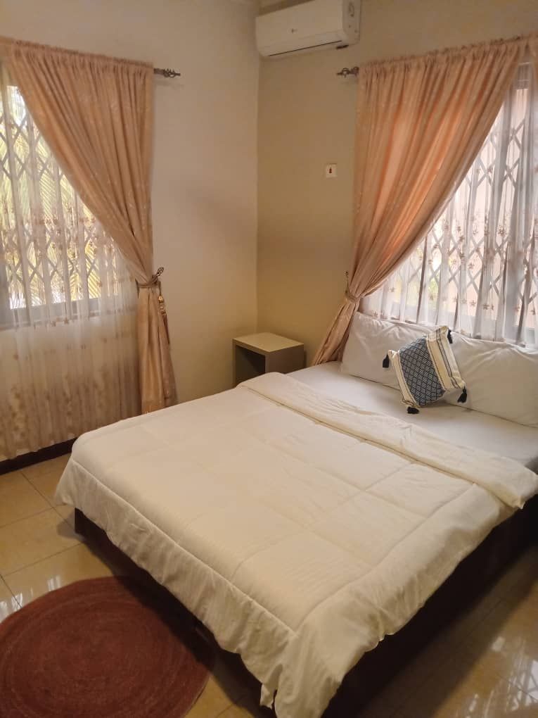 A bedroom with a bed, curtains, a small bedside table, and a red rug.