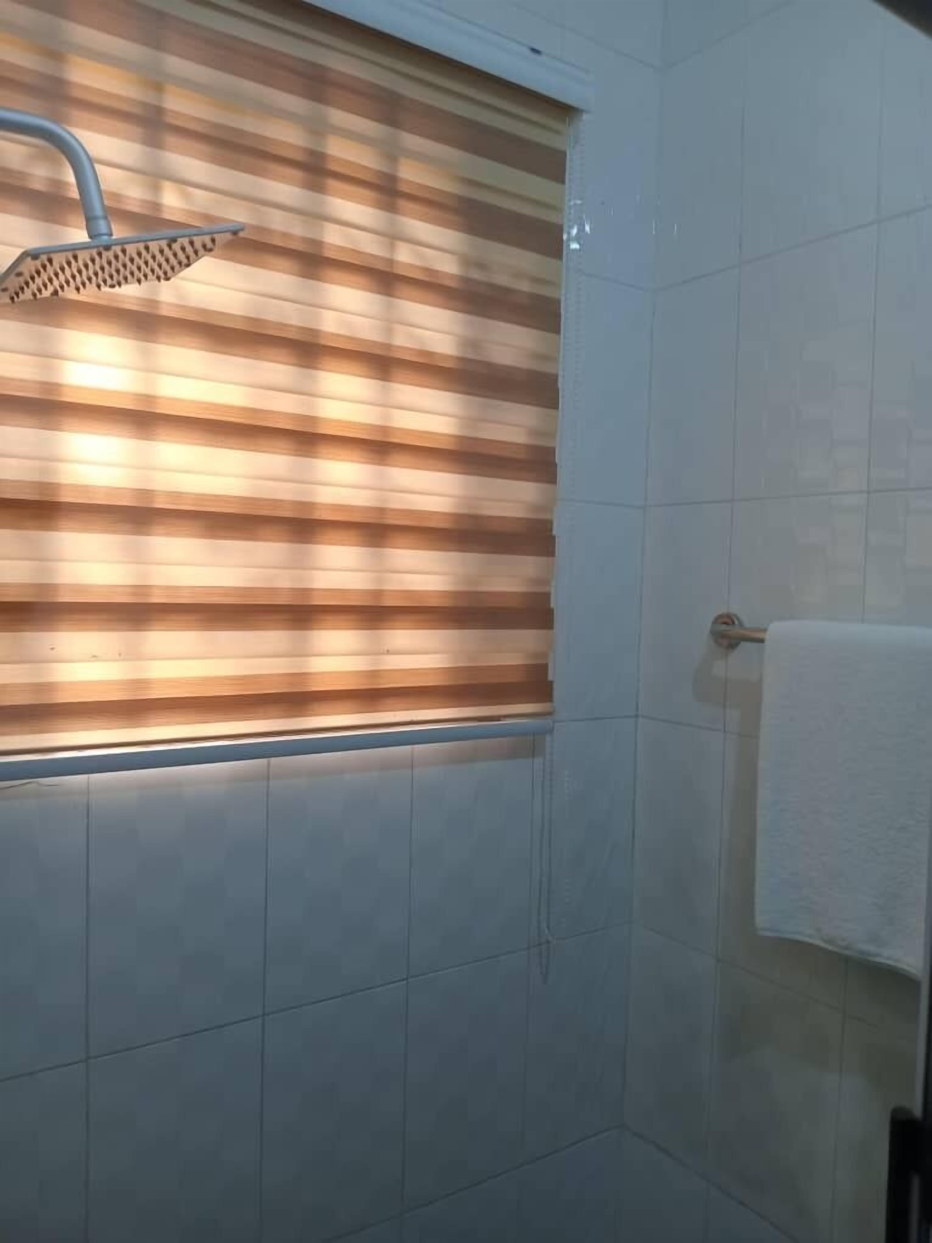Un baño con ducha, paredes de azulejos y una ventana con persianas.