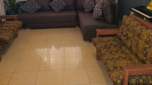 A living room with a sectional sofa, a ceiling fan, and a piano. - Fresh Air Lodge (Accra)