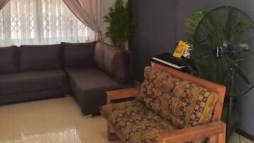 A living room with a dark brown sofa, a patterned armchair, a ceiling fan, a potted plant, and a standing fan.