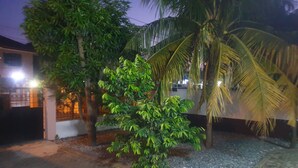 A paved courtyard with a palm tree, a small tree, and a building with a gated entrance. - Fresh Air Lodge (Accra)
