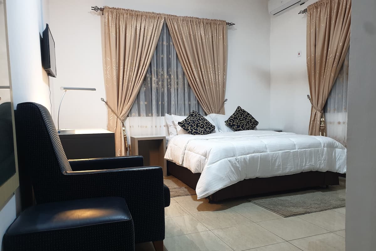 A bedroom with a bed, two chairs, a nightstand, and curtains.
