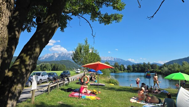 Ein Campingplatz am Seeufer mit Zelten, Picknicktischen und entspannten Menschen am Wasser.