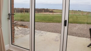 Eine Glastür öffnet sich zu einer Terrasse mit einem Kiesweg und einem grasbewachsen Feld im Hintergrund.