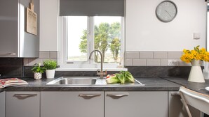 A modern kitchen with a sink, countertop, and window. - Wheal Prosper Lodge (Helston)