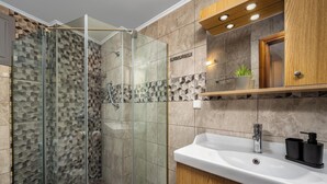A modern bathroom with a glass-enclosed shower, a white sink, and wooden cabinets.