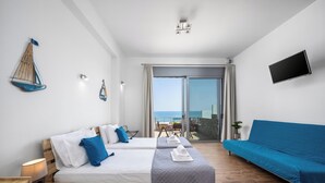 A modern hotel room with a balcony, a bed with blue and white bedding, a blue sofa, and a flat-screen TV mounted on the wall.