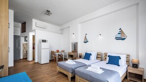 A modern hotel room with two beds, a dining area, and a kitchenette.