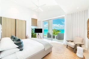 Une chambre moderne avec un grand lit, un téléviseur posé sur un trépied et une vue sur l’océan grâce à de grandes portes vitrées.