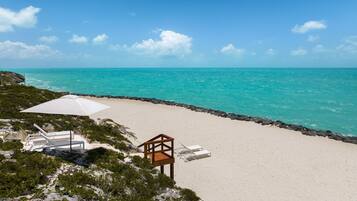 A beach with white sand, a wooden deck, and a white umbrella.