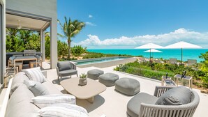 A modern outdoor living area with a pool, lounge chairs, and a view of the ocean. - Ocean Estate Reef 6 Bedroom Including 2 Guesthouse OE17 (Providenciales)