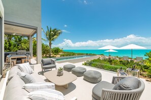 A modern outdoor living area with a pool, lounge chairs, and a view of the ocean.