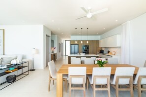 Une cuisine moderne avec des meubles blancs, une table à manger en bois et un ventilateur de plafond.
