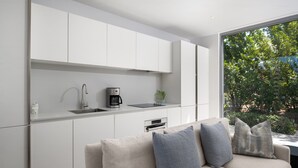 Una cocina moderna con armarios blancos, horno empotrado y cafetera.