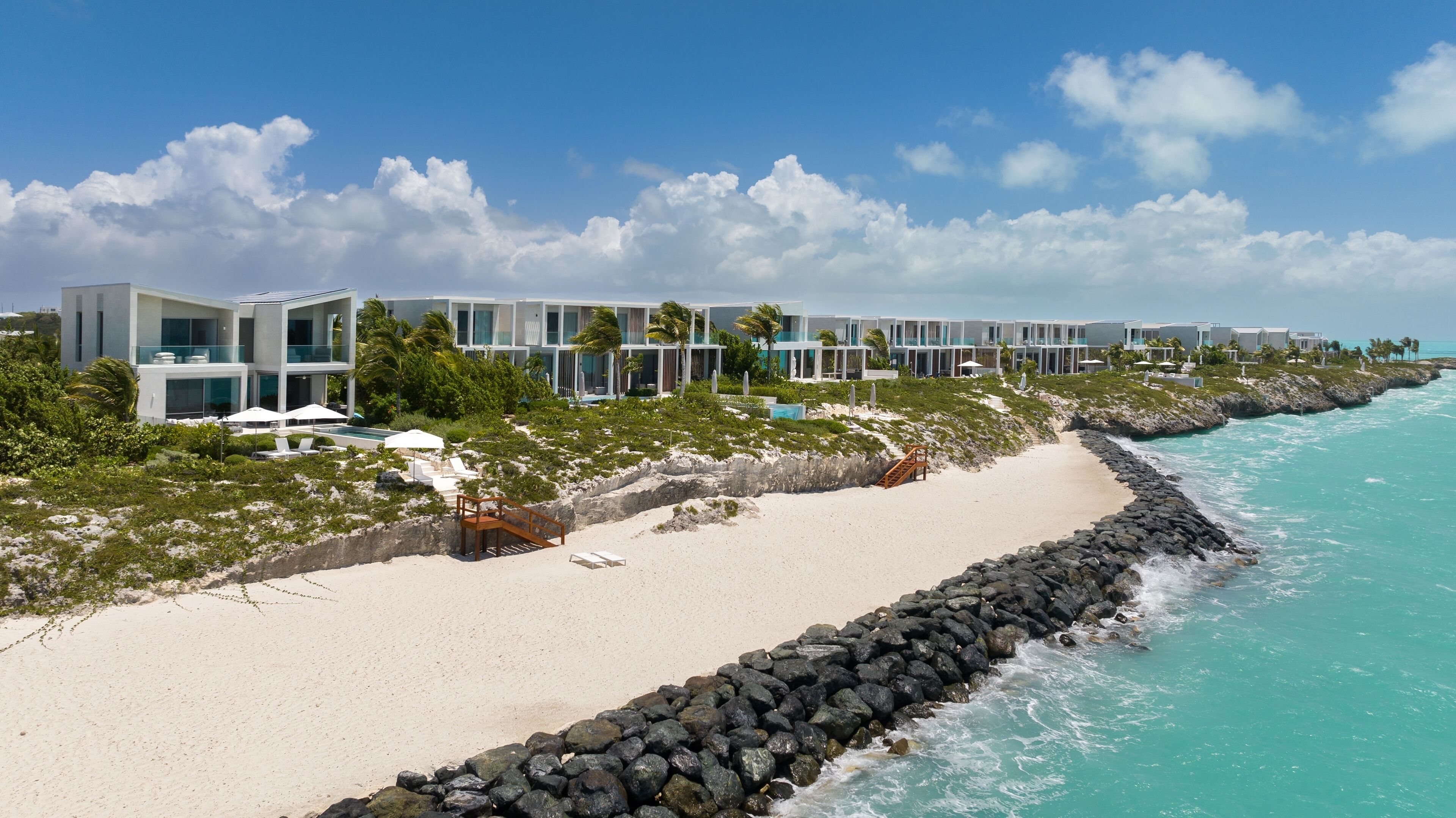 Un hôtel situé sur la côte, doté d’une architecture moderne, d’une plage de sable et d’un rivage rocheux.
