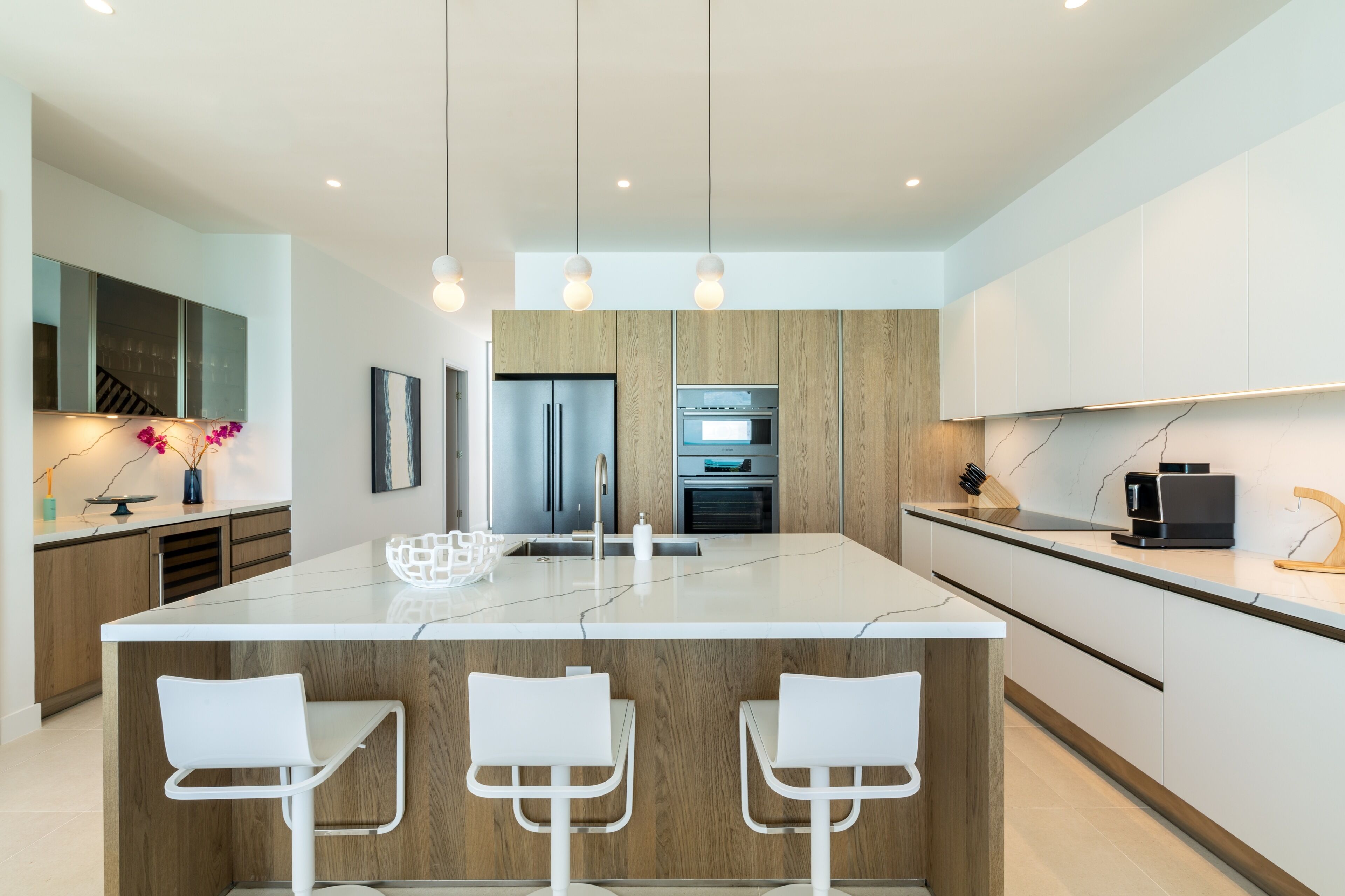 A modern kitchen with a central island, wooden cabinets, stainless steel appliances, and pendant lighting.