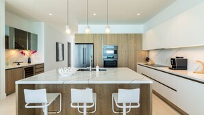 Una cocina moderna con una isla central, armarios de madera, electrodomésticos de acero inoxidable e iluminación colgante.