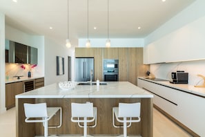A modern kitchen with a central island, wooden cabinets, stainless steel appliances, and pendant lighting. - Ocean Estate Reef 6 Bedroom Including 2 Guesthouse OE17 (Providenciales)