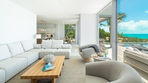 Un salón moderno con un ventanal grande que da a una piscina y al océano.