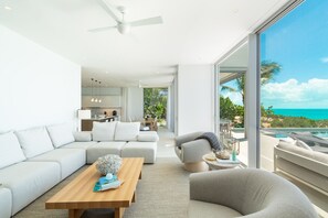 A modern living room with a large window overlooking a pool and ocean. - Ocean Estate Reef 6 Bedroom Including 2 Guesthouse OE17 (Providenciales)