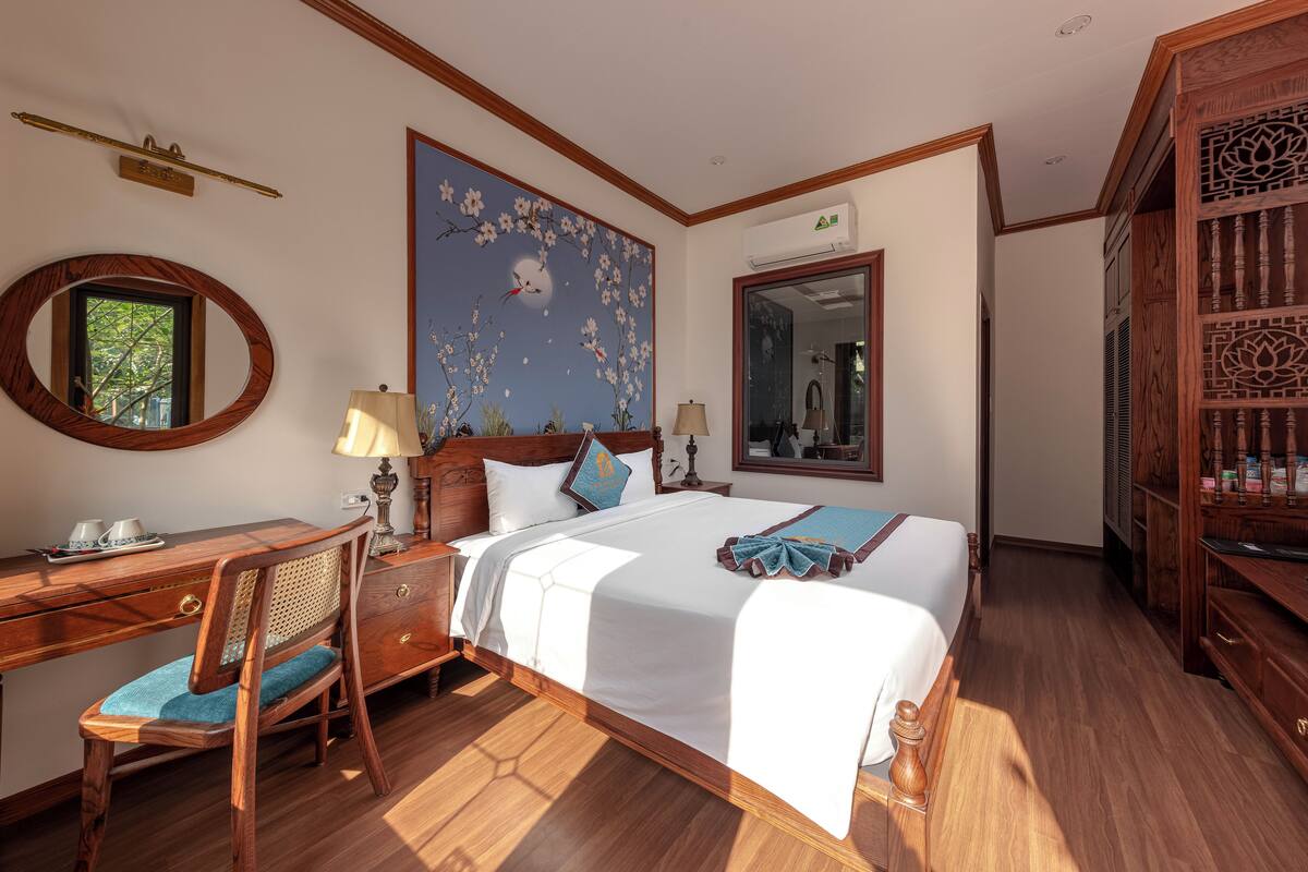 A hotel room with a large bed, wooden furniture, a painting on the wall, and a mirror.