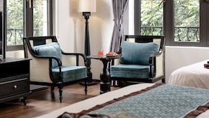 A hotel room with a large bed, two armchairs, a small table with a lamp, and large windows with curtains. - Indochine Boutique Hotel Ninh Binh (Nam Hoa Lu)