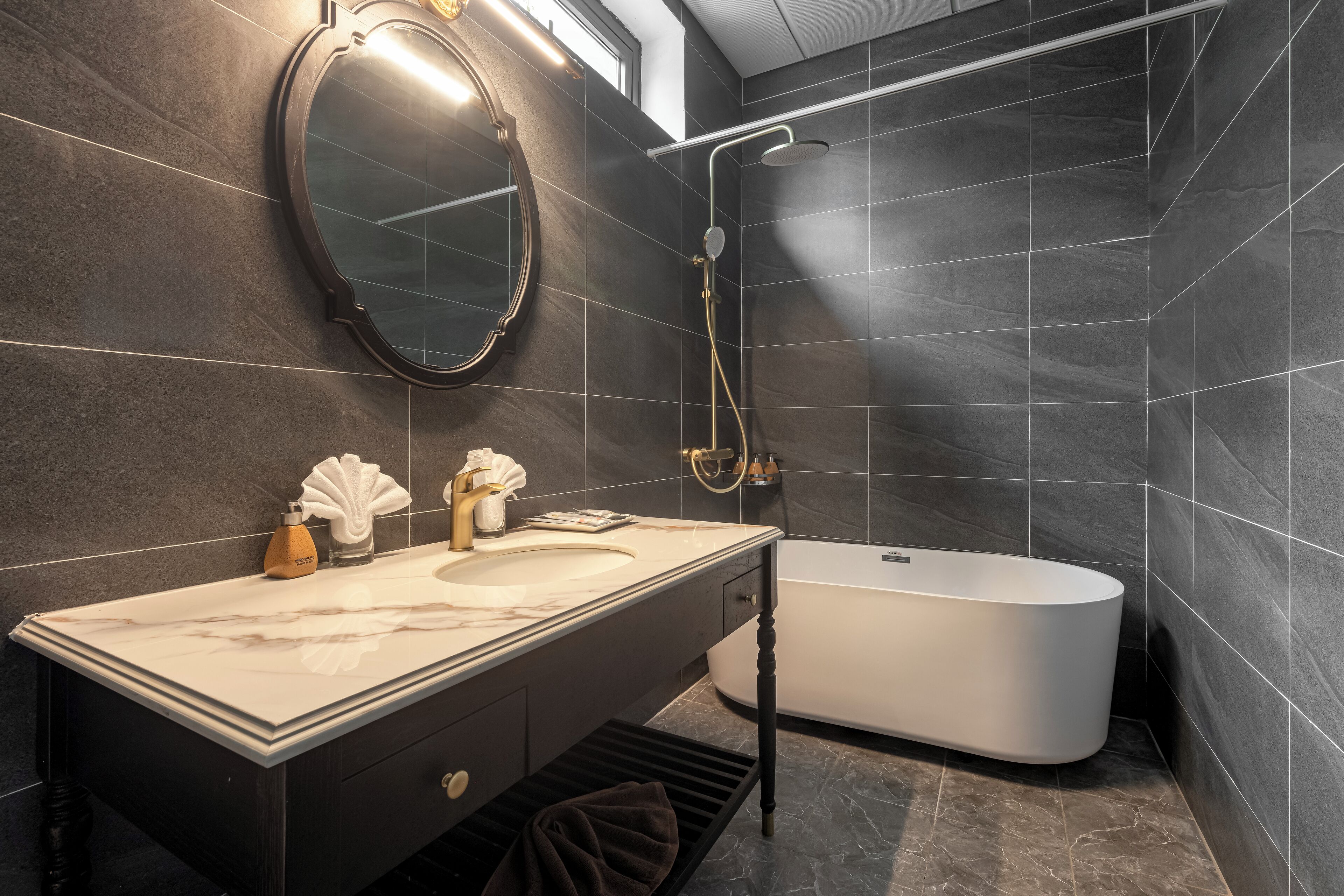 A modern bathroom with a marble vanity, a freestanding bathtub, and dark tiled walls.