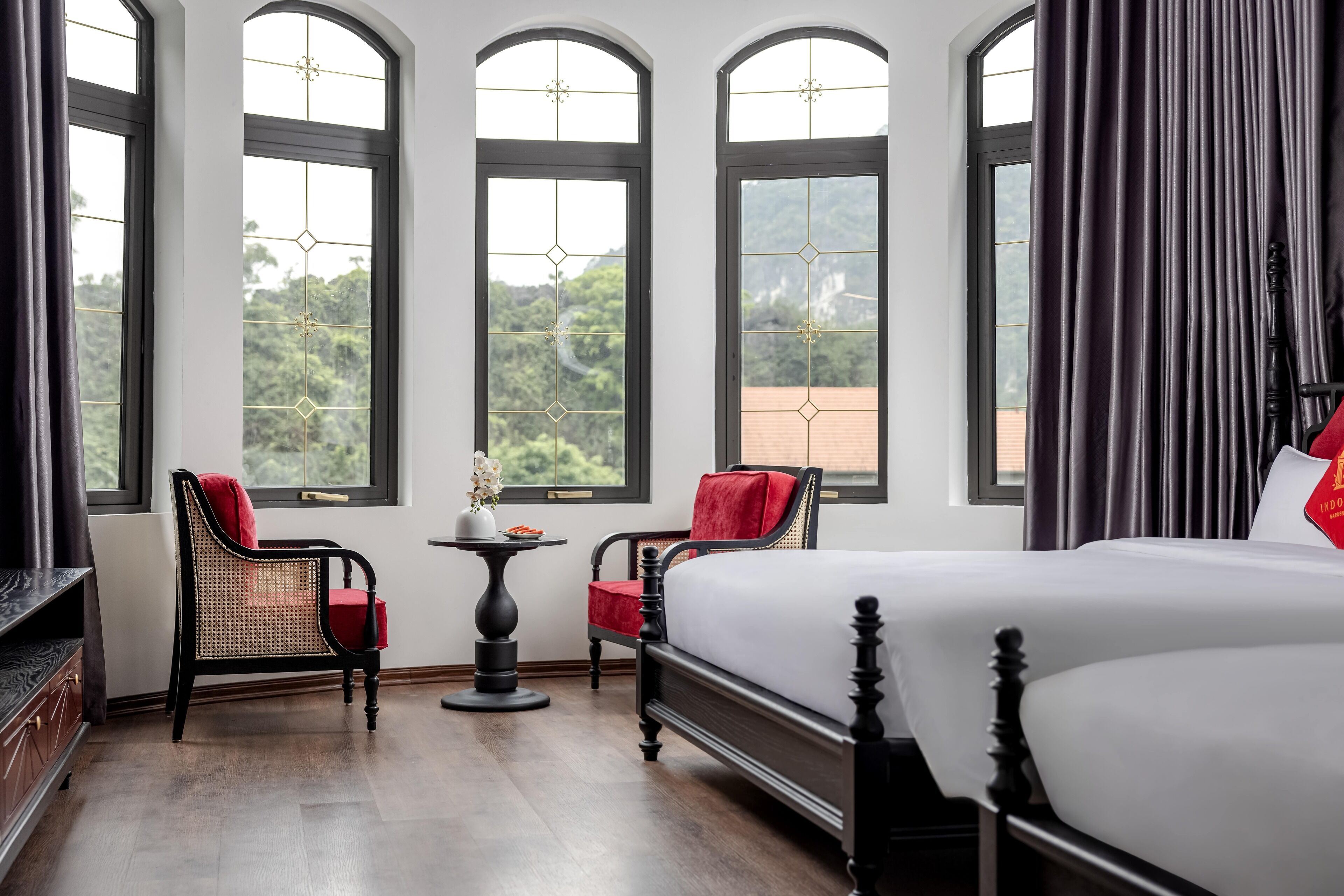 Una camera d'albergo con un letto grande, due poltrone, un tavolino e ampie finestre vista sul verde.