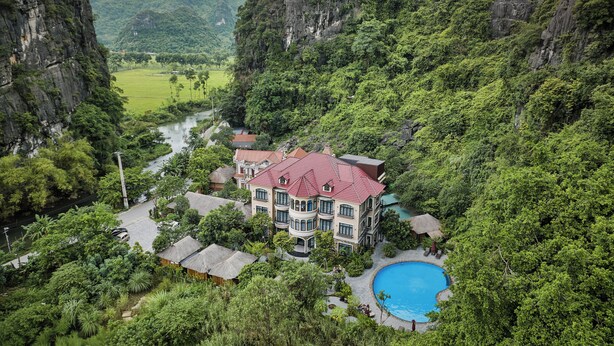 A resort with a swimming pool surrounded by lush greenery and a river. - Indochine Boutique Hotel Ninh Binh (Nam Hoa Lu)