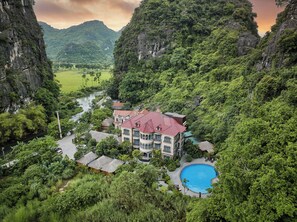 A resort with a swimming pool surrounded by lush greenery and a river.
