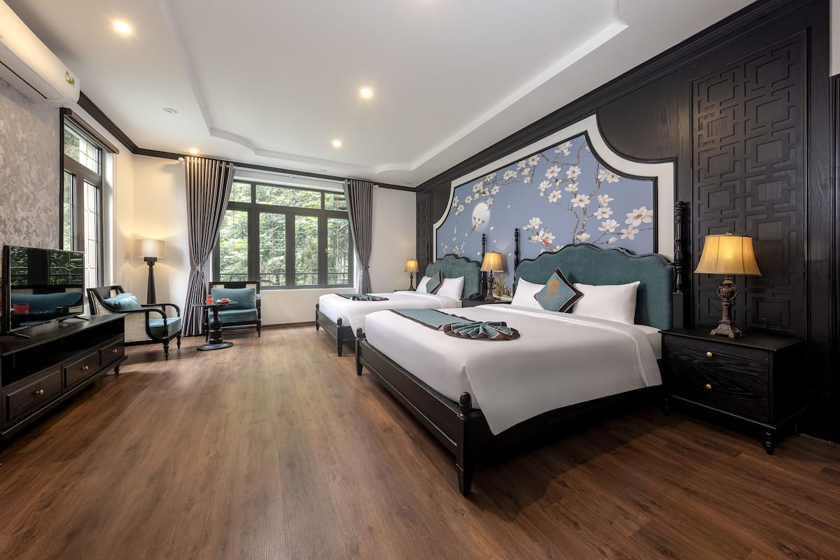 A hotel room with two beds, a TV, a desk, and a window with curtains.