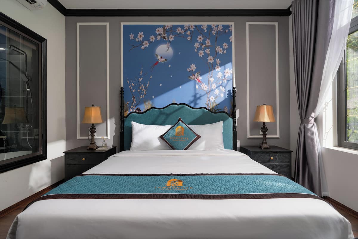 A hotel room with a large bed, two bedside tables with lamps, a wall mural, and a window with curtains.