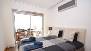 Ein Hotelzimmer mit einem großen Bett, einer Schiebetür zu einem Balkon mit Tisch und Stühlen sowie einer Decken-Klimaanlage.
