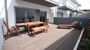 Eine Außenpatio mit Holztisch und Stühlen, einem Liegestuhl und einem kleinen Tisch mit einer Bank.