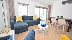 Ein modernes Wohnzimmer mit einem grauen Sofa, einem kleinen runden Couchtisch und einem Essbereich mit Tisch und Stühlen.