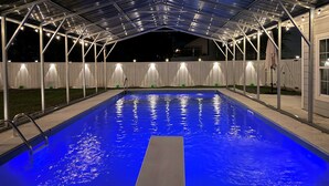 Ein Pool im Freien mit überdachtem Bereich, umgeben von einem weißen Zaun und beleuchtet mit Lichterketten.