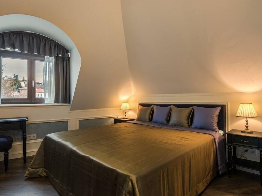 A bedroom with a large bed, two bedside tables with lamps, a desk, and a chair.
