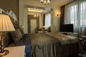 Habitación de hotel con una cama grande, televisión, escritorio y una silla. Hay un espejo en la pared y una puerta que da a otra habitación.