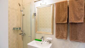 Un baño con cabina de ducha de vidrio, un lavamanos blanco con un jabonera verde y dos toallas marrones colgadas en un perchero.