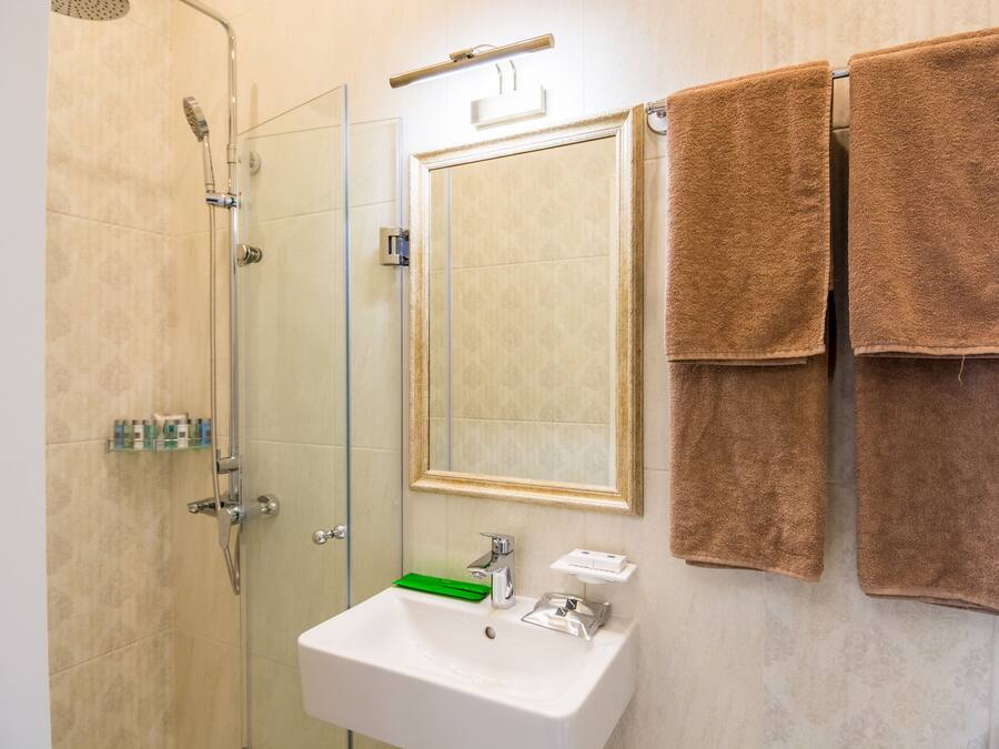 Un baño con cabina de ducha de vidrio, un lavamanos blanco con un jabonera verde y dos toallas marrones colgadas en un perchero.