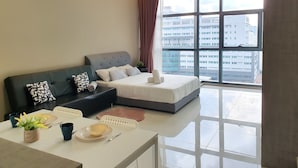 A modern hotel room with a large window, a sofa, a bed, and a dining area with a table and chairs.