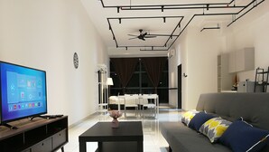 A modern living room with a flat-screen TV, a sofa, a coffee table, and a dining area with a table and chairs.