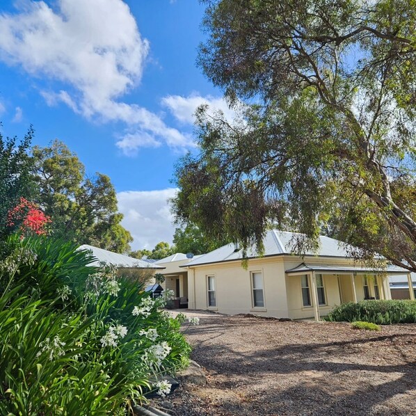 A two-story house with a covered driveway, surrounded by lush greenery and flowering plants. - Bassett House Willunga - An entire spacious home on a tree lined street.  (Willunga)