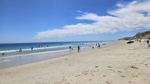 Una playa con gente, cielo despejado y un acantilado lejano.