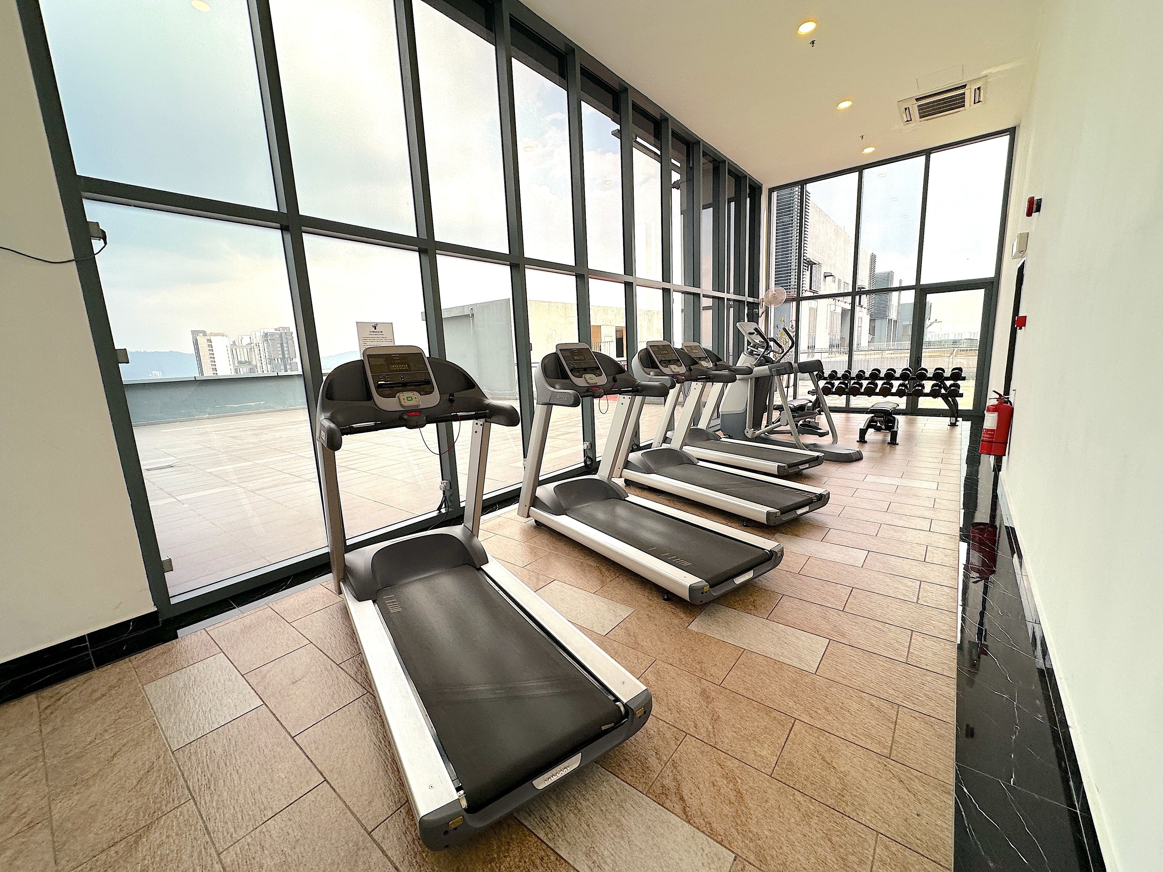 Une salle de sport équipée de tapis de course et d’haltères, dotée de grandes fenêtres et offrant une vue sur un plan d’eau.